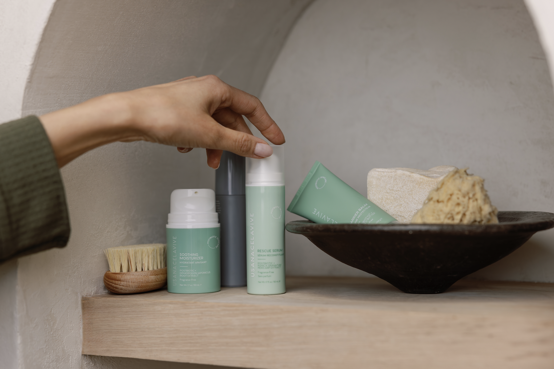 female hand reaching for postbiotic skincare bottles on shelf